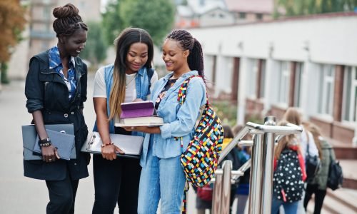 Three african students female posed with backpacks and school items on yard of university and look at tablet.